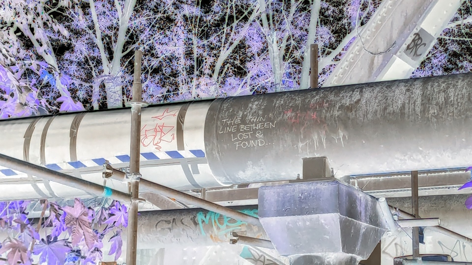 A piece of graffiti underneath a bridge in Emu Plains, New South Wales. It reads 'THE THIN LINE BETWEEN LOST & FOUND...'. A colour inversion filter has been applied.