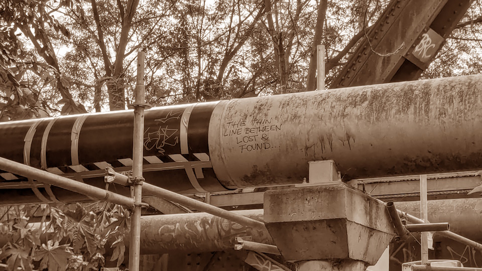 A piece of graffiti underneath a bridge in Emu Plains, New South Wales. It reads 'THE THIN LINE BETWEEN LOST & FOUND...'. A sepia filter has been applied.