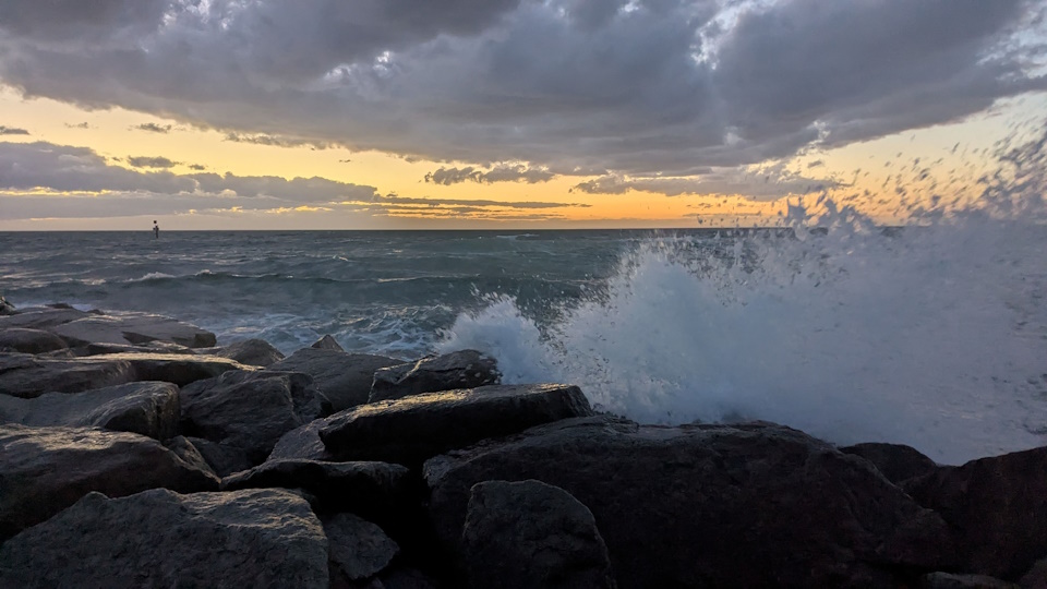 During a rough tide after the sun has set, waves crash against rocks on the shore at Carrum Beach.